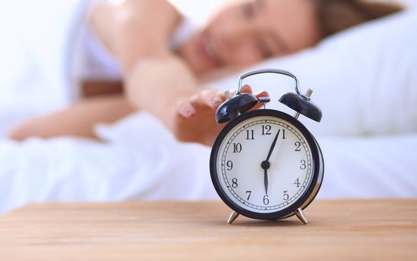 Young sleeping woman and alarm clock in bedroom at home - Photo, Image