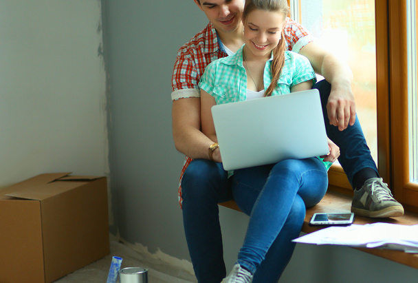 Portrait of young couple moving in new home sitting with laptop - Фото, изображение