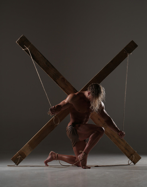 Sexual naked man, muscular, hands tied rope to wooden beams - Foto, afbeelding