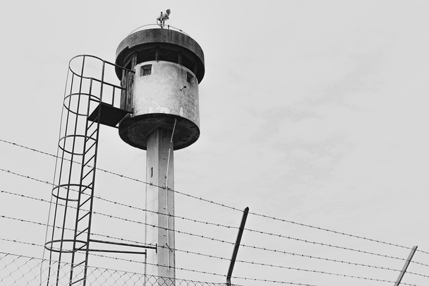 Abandoned sentry box tower isolated by a net with barbed wire. - Photo, Image