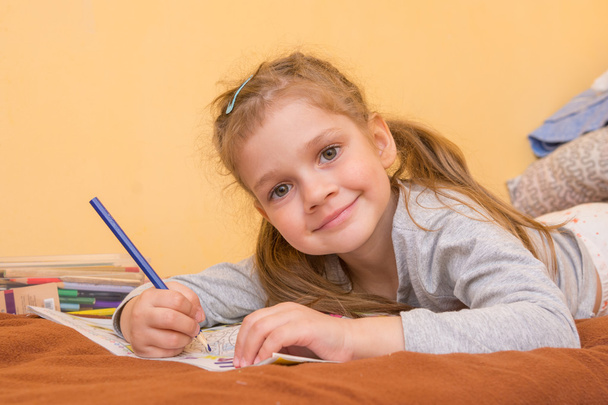 Iloinen pikkutyttö piirtää makaa vatsallaan kynä paperilla
 - Valokuva, kuva