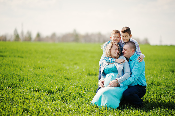 Gelukkige zwangere familie met twee zonen, gekleed in een turquoise stolsel - Foto, afbeelding