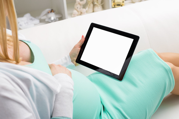 Pregnant woman sitting on sofa and using blank screen tablet - Fotó, kép