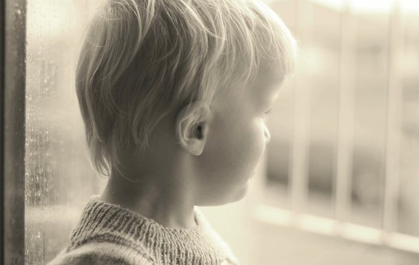 kleiner Junge, der im geöffneten Fenster steht und den Garten im Regen beobachtet. Schwarz-weiße Version - Foto, Bild