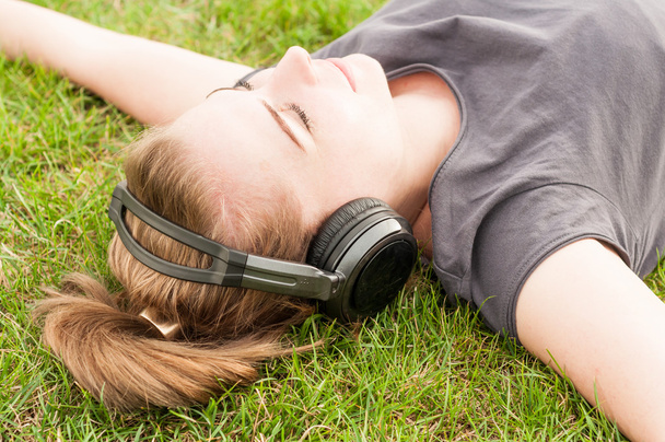 Beautiful woman in closeup lying on grass and listen music - Photo, Image