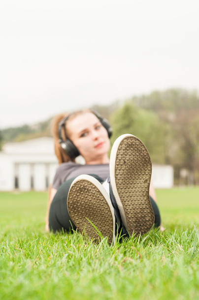 Молодая женщина слушает музыку лежа скрестив ноги на траве
 - Фото, изображение