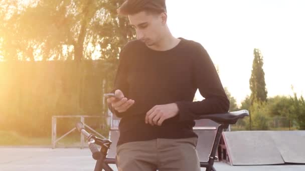 Όμορφος άντρας τύπο ένα μήνυμα στέκεται κοντά σε ένα ποδήλατο κατά το ηλιοβασίλεμα. - Πλάνα, βίντεο