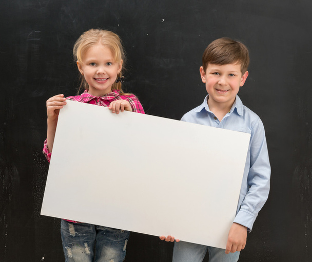 two smiling schoolchildren with blank sheet of paper - Foto, afbeelding