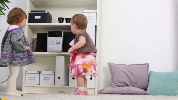 Two happy little girls stand near shelves with music center - Záběry, video