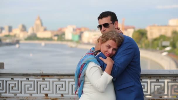 Pretty woman in white and young man embrace on bridge - Filmmaterial, Video