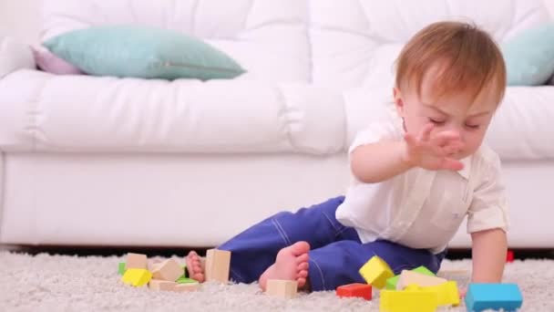 Cute baby sits on soft carpet and breaks tower of tinker toys - Felvétel, videó