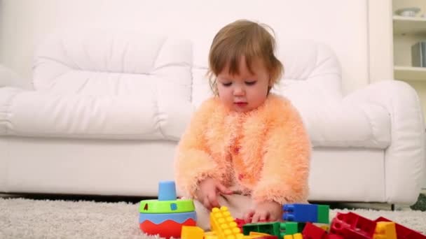 Cute little girl sits on carpet and plays with tinker toys - Filmmaterial, Video