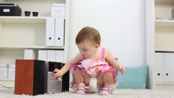 Little girl touches stereo system on carpet in room at home - Záběry, video