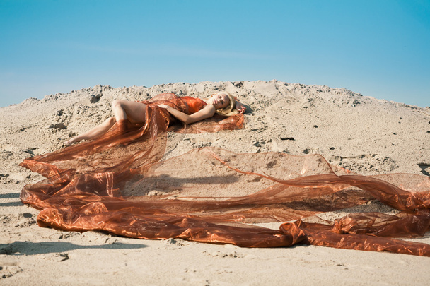 Girl lying on sand in orange cloth - Fotó, kép