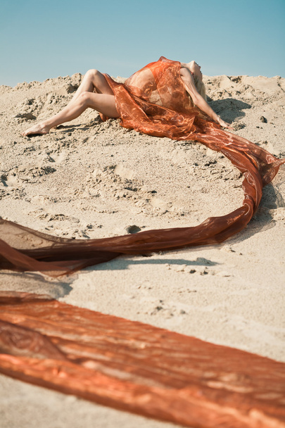 Girl lying on sand in orange cloth - Fotoğraf, Görsel