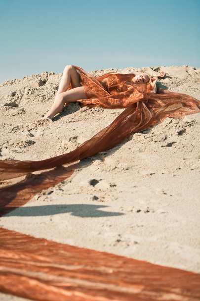 Girl lying on sand in orange cloth - Fotoğraf, Görsel