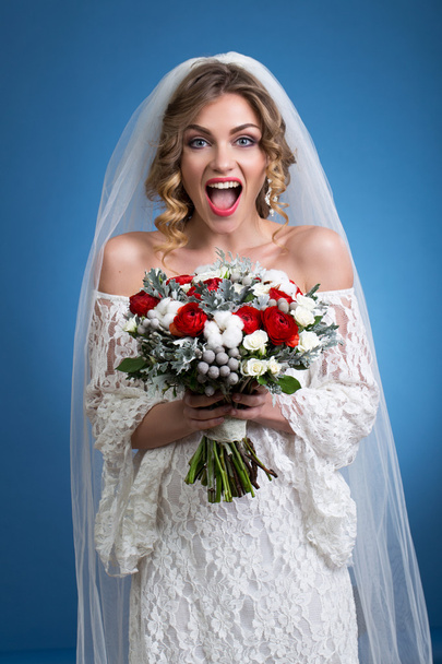 young beautiful girl in a wedding dress with a veil with a bouquet of flowers in hands on blue background - Foto, immagini