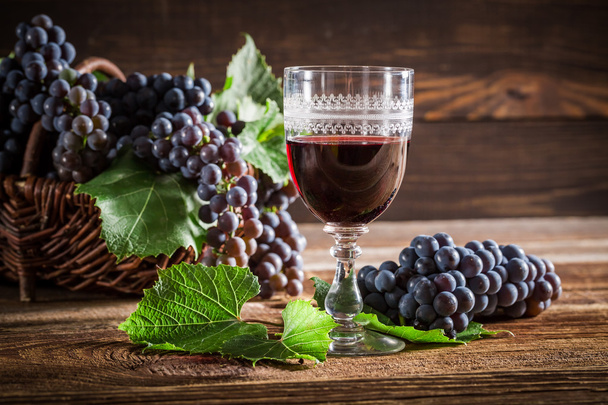 Νόστιμο κόκκινο κρασί με σταφύλια στο ψάθινο καλάθι - Φωτογραφία, εικόνα