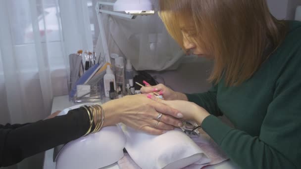 Manicurist odłożyć szelak pokrycie z gwoździ kobiety w salonie piękności przez pomarańczowy kij. Korekcji - Materiał filmowy, wideo