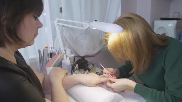 Profesjonalny Manikiurzystka odłożyć basic z powierzchni paznokci klienta w salon piękności przez orange stick - Materiał filmowy, wideo