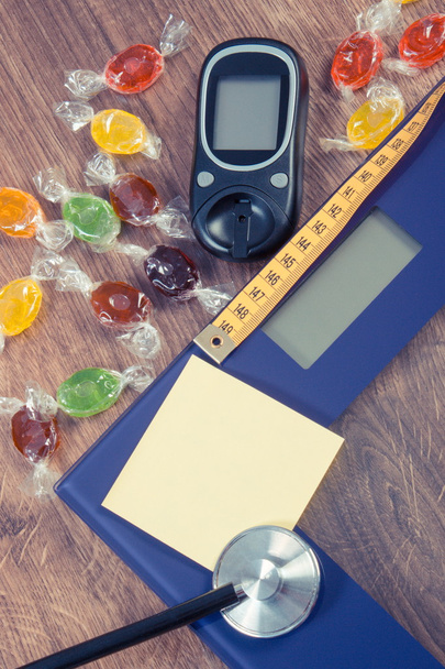 Elektroninen kylpyhuone mittakaavassa, glukometri, stetoskooppi ja senttimetri värikkäitä makeisia, diabetes, laihtumiseen ja vähentämiseen syöminen makeisia
 - Valokuva, kuva