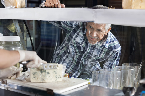 Man Watching Salesman Slicing Blue Cheese In Shop - Фото, изображение