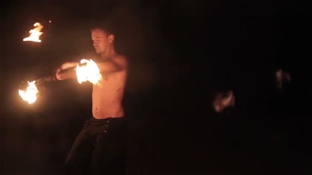 Fire show performance. Handsome male fire performer twirling and tossing up fire baton staff ignited from both sides. Slow motion - Footage, Video