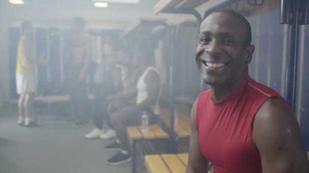 uśmiechnięty mężczyzna siedzi w szatni siłowni - Materiał filmowy, wideo