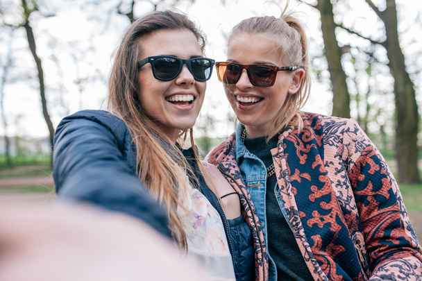 Two girl sitting on the bech in the park and taking selfie. - Valokuva, kuva