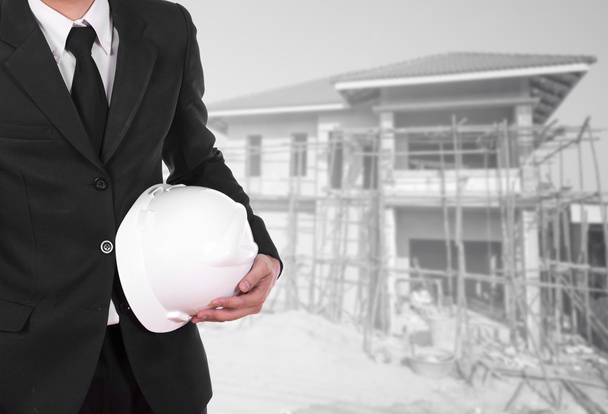 Инженер, держащий шлем на фоне строительства дома
 - Фото, изображение