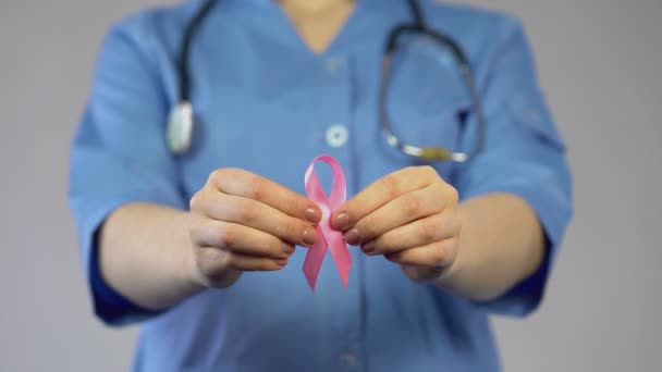 Female in blue coat holding pink ribbon in hands and warning about breast cancer - 映像、動画