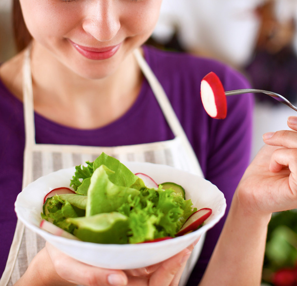 Giovane donna mangiare insalata fresca in cucina moderna - Foto, immagini