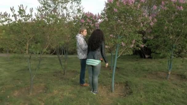 Dwie dziewczyny wąchanie kwiatów bzu w zielonym parku - Materiał filmowy, wideo
