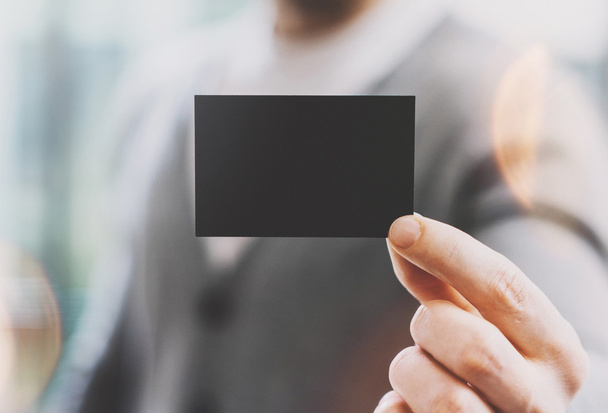 Man wearing casual shirt and showing blank black business card. Blurred background. Ready for private information. Horizontal mockup, film effect - Fotoğraf, Görsel