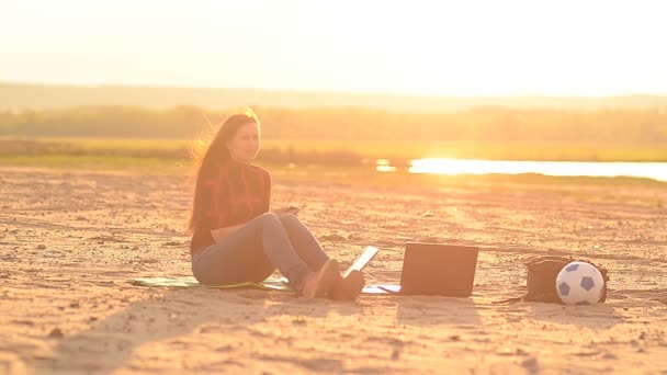 Dziewczyna na plaży rozmawia przez telefon o zachodzie słońca - Materiał filmowy, wideo