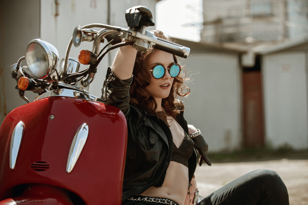 Portret van een mooi meisje in lederen jas, Brasserie en glazen in de buurt van rode motorfiets - Foto, afbeelding
