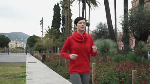 Young woman running in the park with palm trees exotic shrubs and flowers. - Imágenes, Vídeo