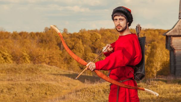 Ρωσική Τοξότης με το ξύλινο τόξο στο παραδοσιακό κόκκινο κοστούμι και f - Φωτογραφία, εικόνα