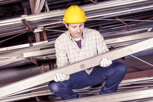 Junger Metallarbeiter kontrolliert Metallstangen in Stahlwerk - Foto, Bild