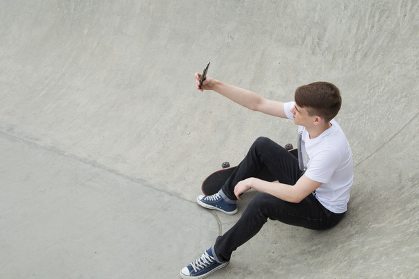Young man sitting near skate board using smart phone - Foto, Imagen