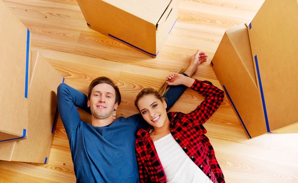 Happy couple lying on the floor in new home with cordboard boxes around - Foto, Imagem