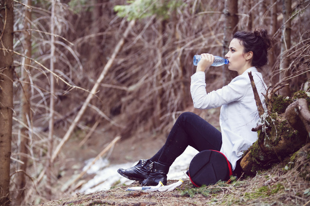 Young woman trekker resting and drinking water in the forest - Foto, imagen