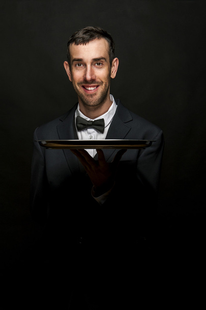 Waiter in black suit holding tray over black background. - Photo, Image