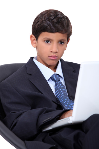 Serious young boy in an adult business suit with a laptop computer - Fotoğraf, Görsel