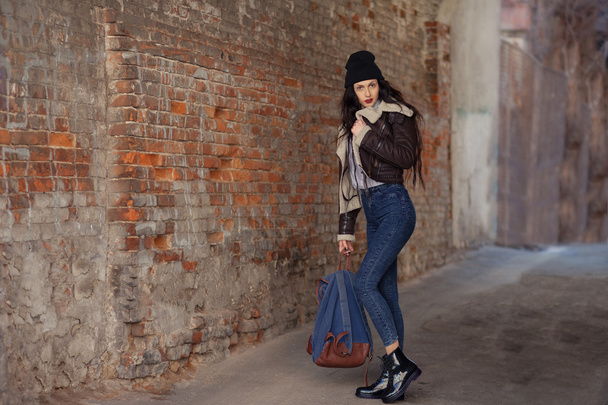 Outdoor lifestyle portrait of pretty young girl, wearing hipster swag grunge style on urban background. Wearing hat and jeans with backpack. Spring fashion woman. Toned style instagram filters. - Photo, Image