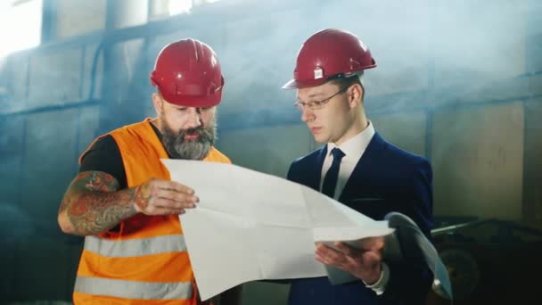 Архитектор и строитель в шлеме с бородой вместе изучают чертежи на строительной площадке
 - Кадры, видео