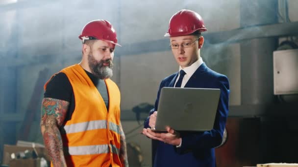 Kask ve sakallı inşaat işçisi bir ambar veya inşaat site içinde laptop ile mühendis - Video, Çekim