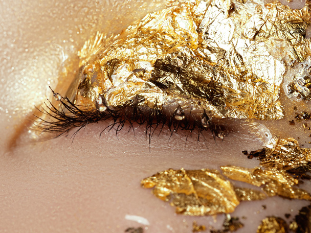 Cosmetics and make-up. Closeup macro shot of fashion sparcle visage. Closeup portrait of beautiful young woman with golden foil on face. Creative makeup.  - Fotó, kép