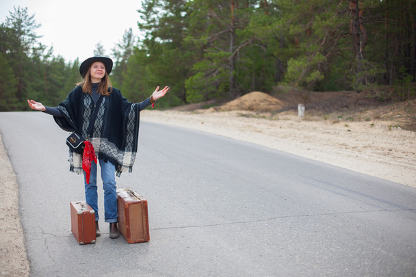 Ein junges Mädchen im Poncho mit Koffer steht auf der Straße - Foto, Bild