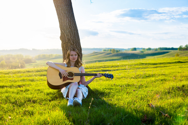 Beautiful young girl playing guitar in the field.  - 写真・画像